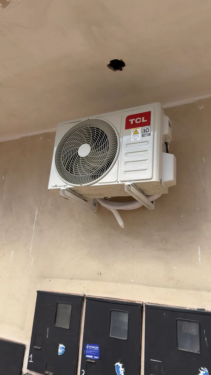 Condensadora TCL instalada na parede, acima de uma fileira de caixas de medidor de energia.