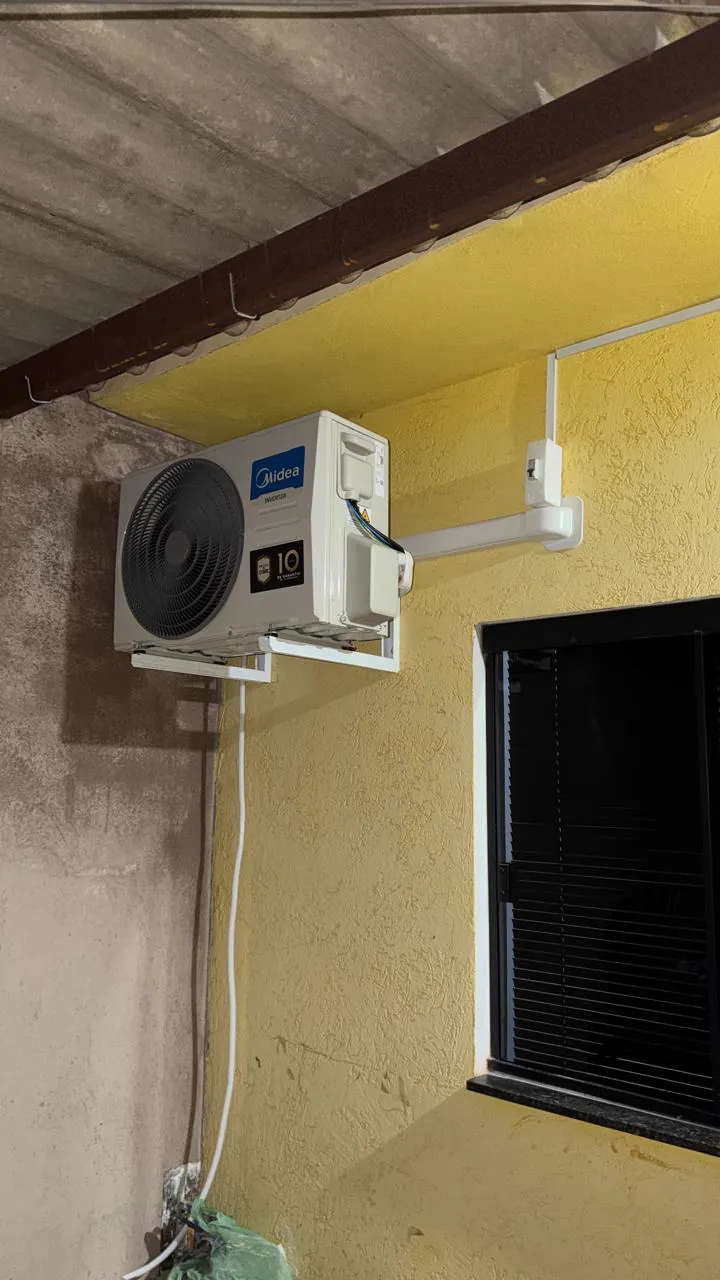 Condensadora instalada em suporte numa parede amarela, ao lado de uma janela.
