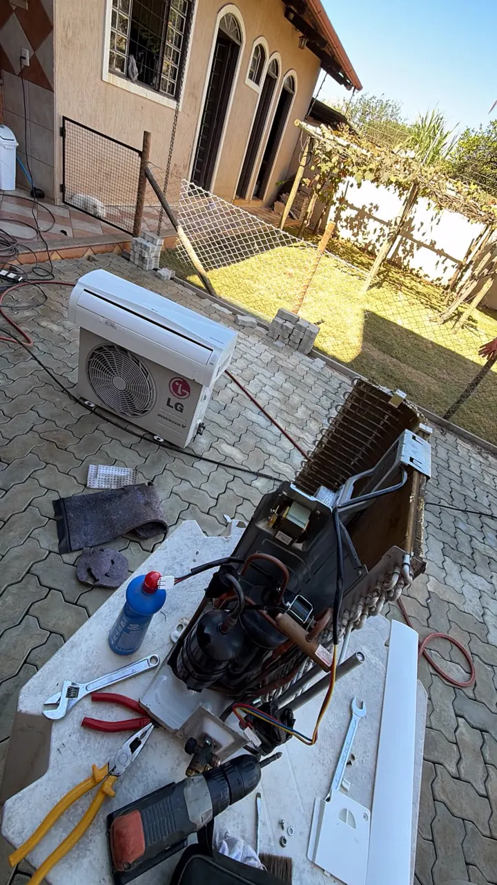 Peças de um ar-condicionado desmontado sobre uma bancada, com alicates, chave e furadeira.