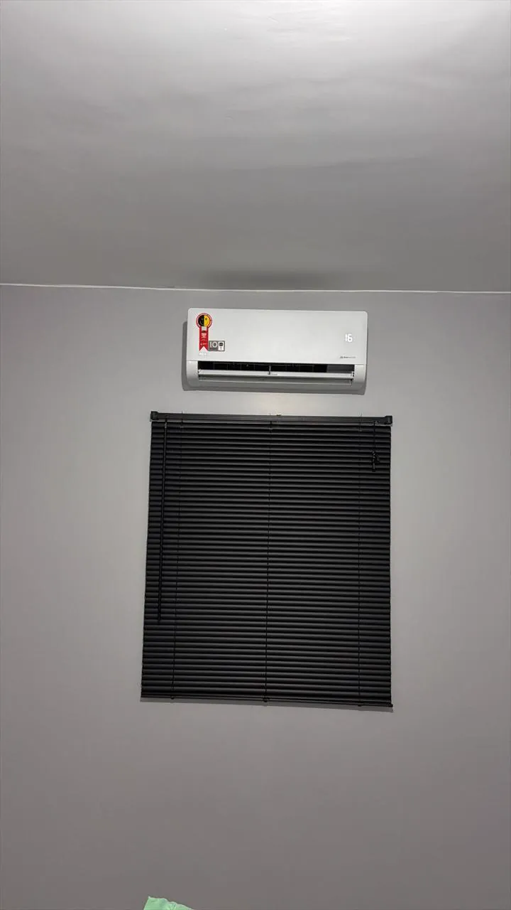 Split instalado acima de uma janela com persiana preta, em parede cinza.